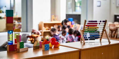Toys in the forefront and preschoolers (blurred out) in class in the background.