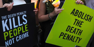 Two demonstrators hold signs that reads "THE DEATH PENALTY KILLS PEOPLE NOT CRIME" and "ABOLISH THE DEATH PENALTY."