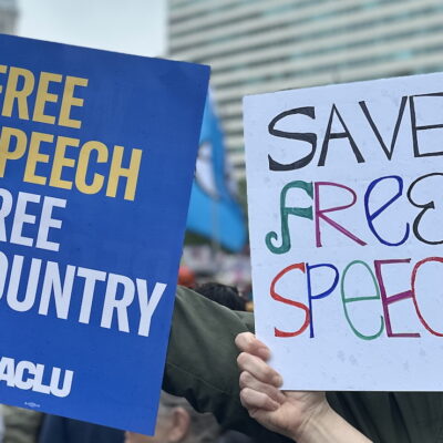One protest sign reads: "Free Speech, Free Country." The other reads: "Save Free Speech"