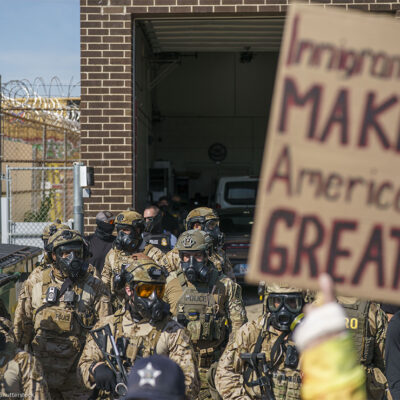 Heavily armed ICE and Border Patrol agents guard the Broadview ICE facility from peaceful protesters opposed to 'Operation Midway Blitz' in Chicagoland; their sign reads 'Immigrants Make America Great'