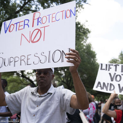 An individual at a demonstration, holding a sign that says "Voter Protection, Not Suppression."